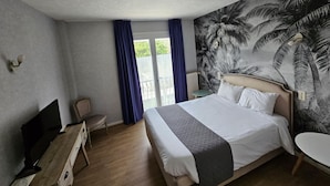Habitación de hotel con una cama grande, un televisor de pantalla plana, un escritorio y una silla. Tiene un balcón con vistas a zonas verdes.