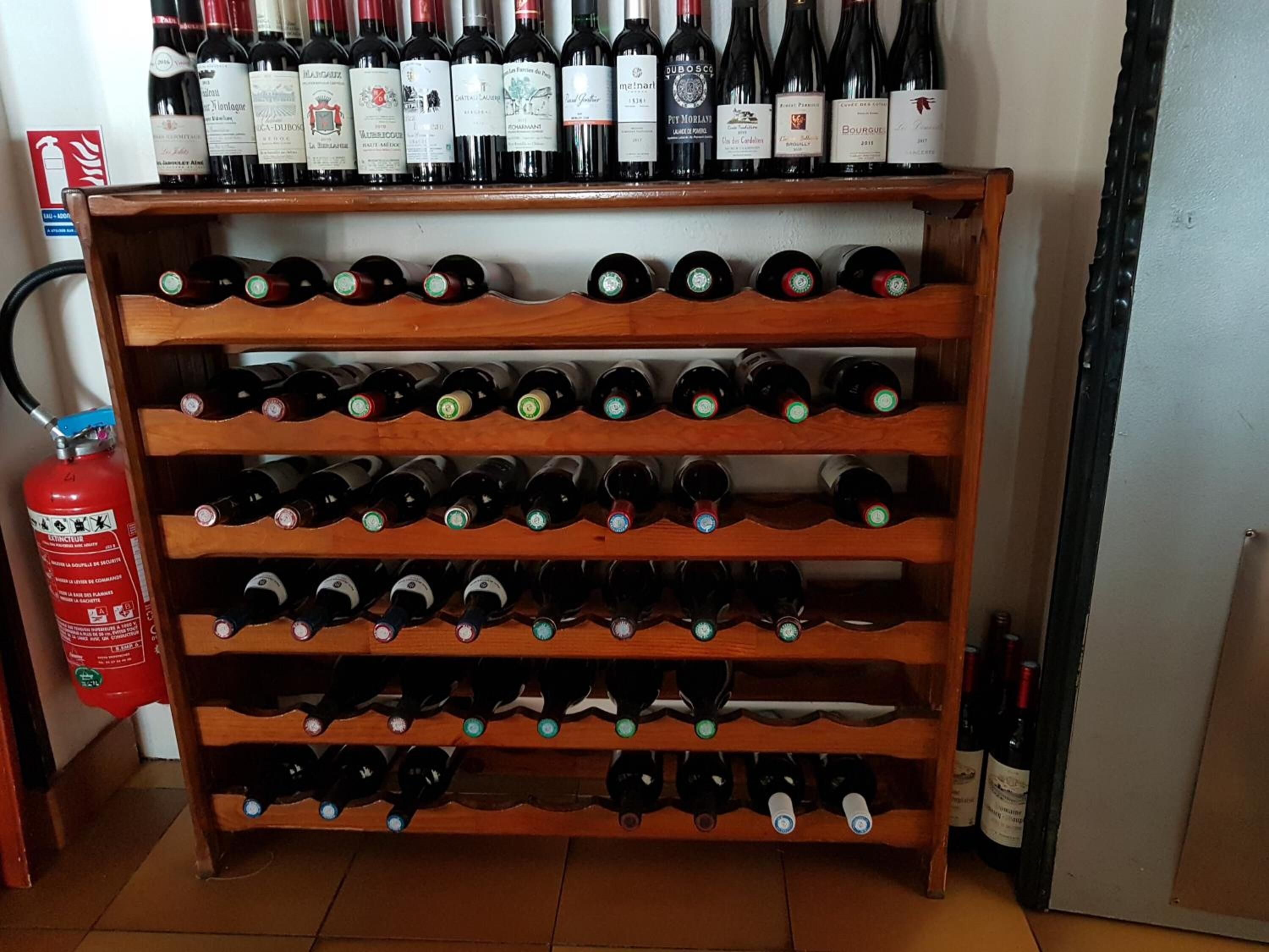 Un meuble à bouteilles contenant de nombreuses bouteilles de vin, un extincteur et un mur décoré de différentes bouteilles de vin.