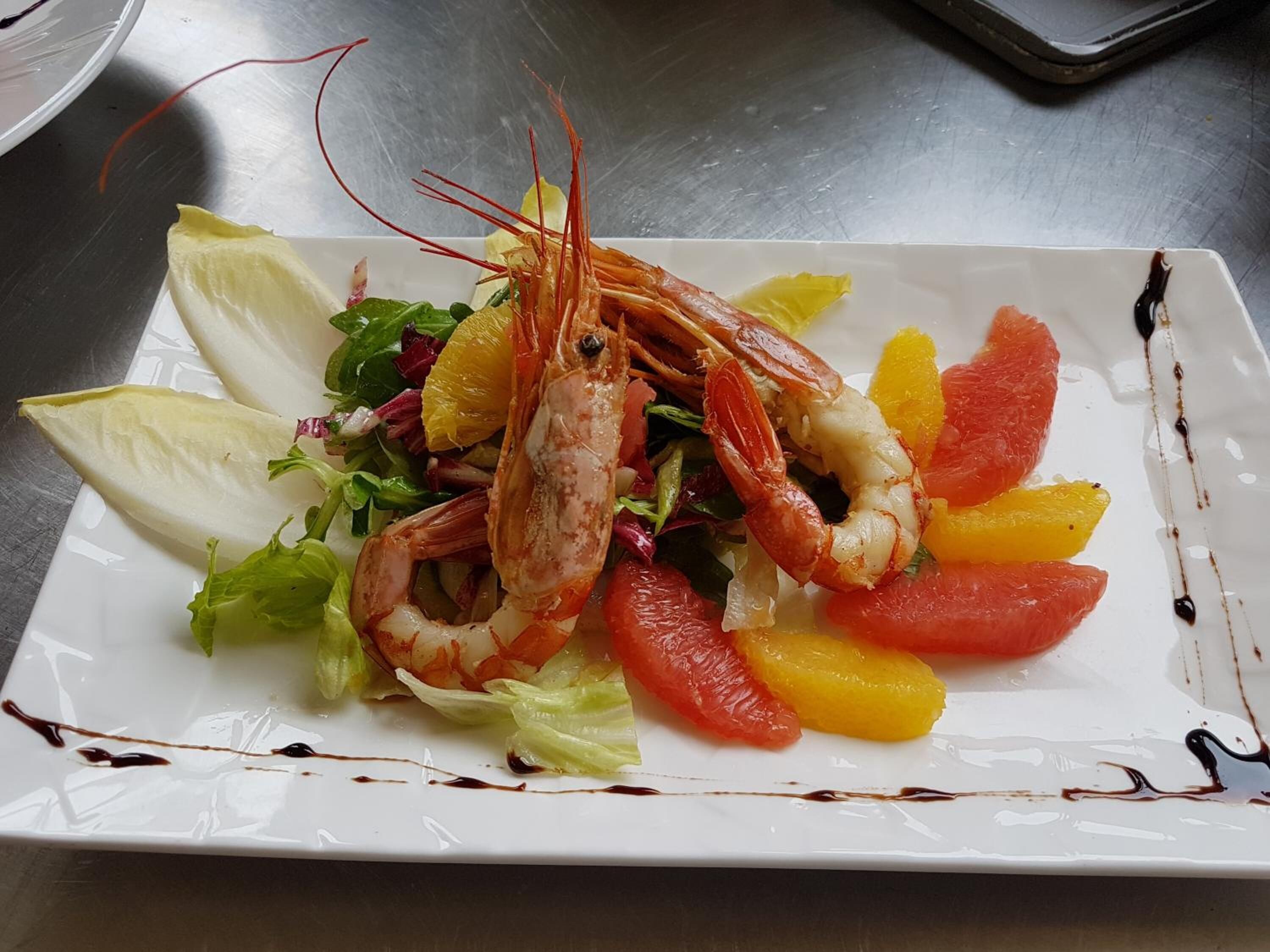 A plate with a cooked shrimp, lettuce, and sliced citrus fruits.