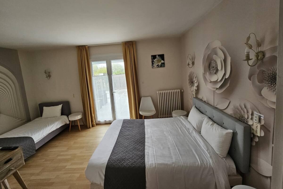A hotel room with a large bed, two single beds, a small table, a chair, and a radiator.