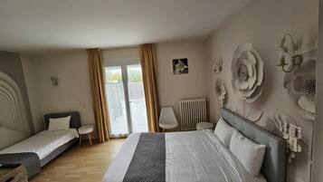 A hotel room with a large bed, two single beds, a small table, a chair, and a radiator.