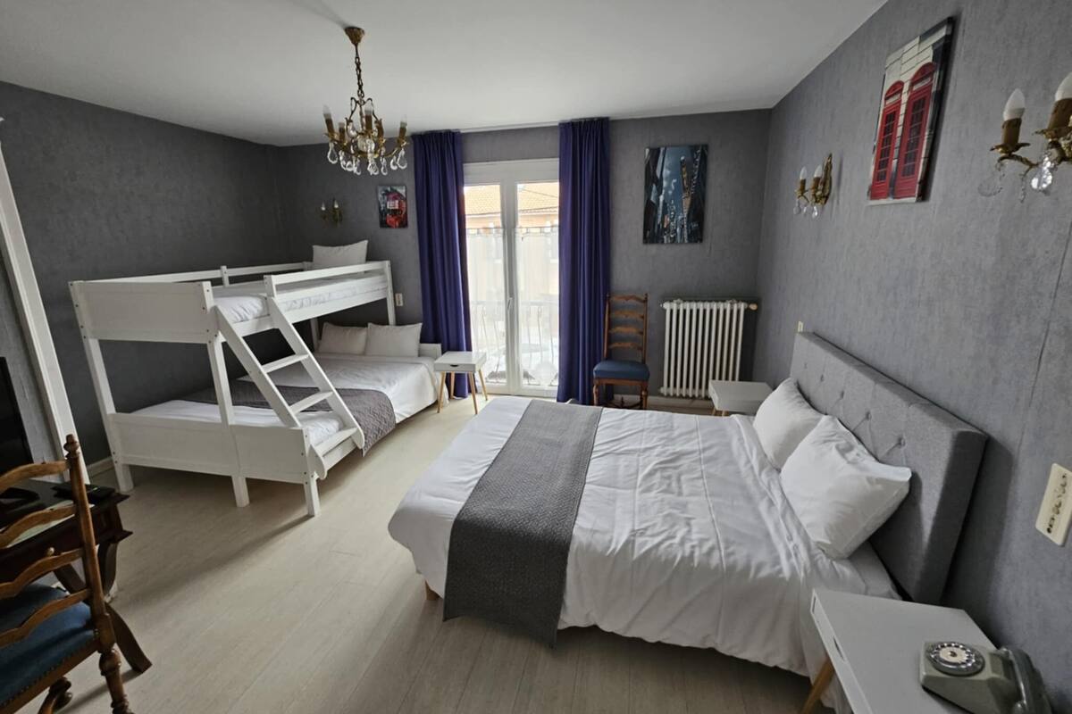 A bedroom with a bunk bed, a single bed, a chair, a small table, a radiator, and a chandelier.
