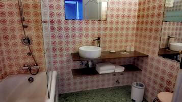 Een badkamer met behang met een patroon, een witte wastafel, een spiegel, een handdoekhouder en een prullenbak.
