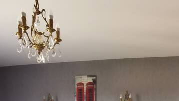 Een slaapkamer met een groot bed, nachtkastjes, een kroonluchter en een rode telefooncel aan de muur.
