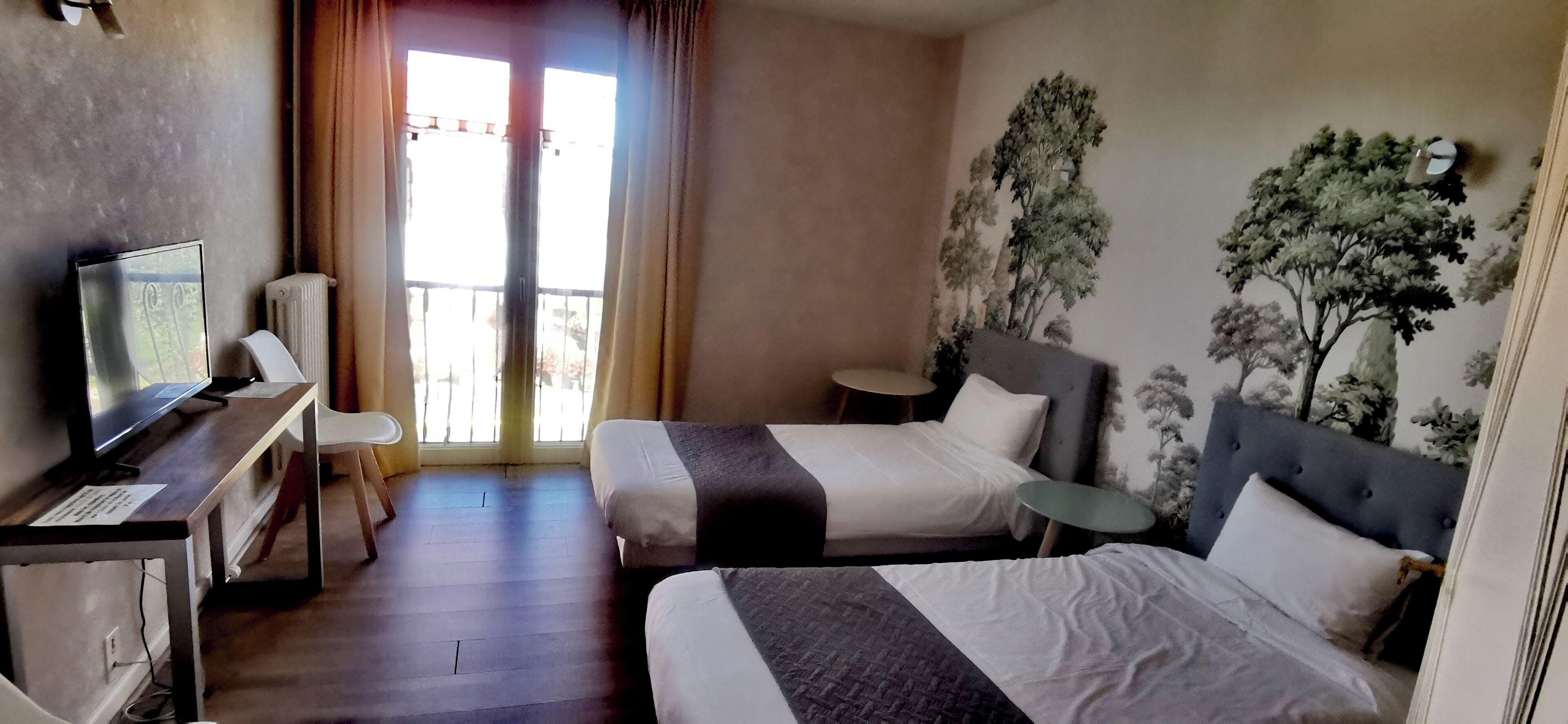 Habitación de hotel con dos camas, un escritorio con computadora, una mesita redonda y un balcón con cortinas.