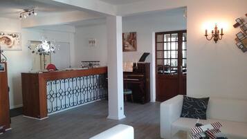 A spacious living area with a piano, a reception desk, and a glass coffee table with a model airplane.