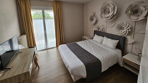 Una habitación de hotel con cama, escritorio, televisor y balcón con cortinas.