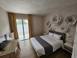 A hotel room with a bed, a desk, a TV, and a balcony with curtains.