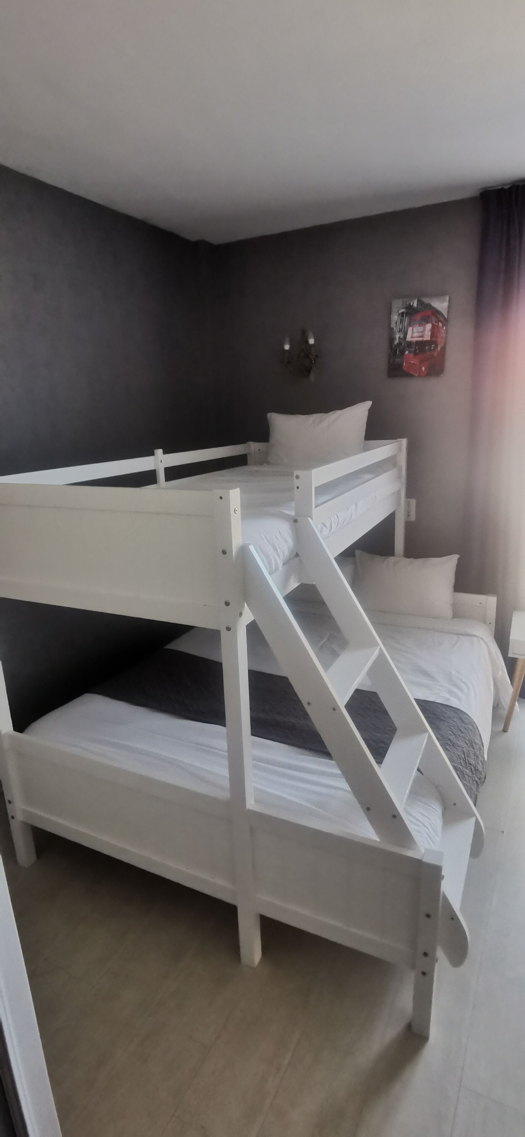 A bunk bed with white metal railings and a grey mattress.