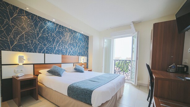 Habitación de hotel con una cama grande, mesitas de noche, un escritorio y un balcón con vistas.