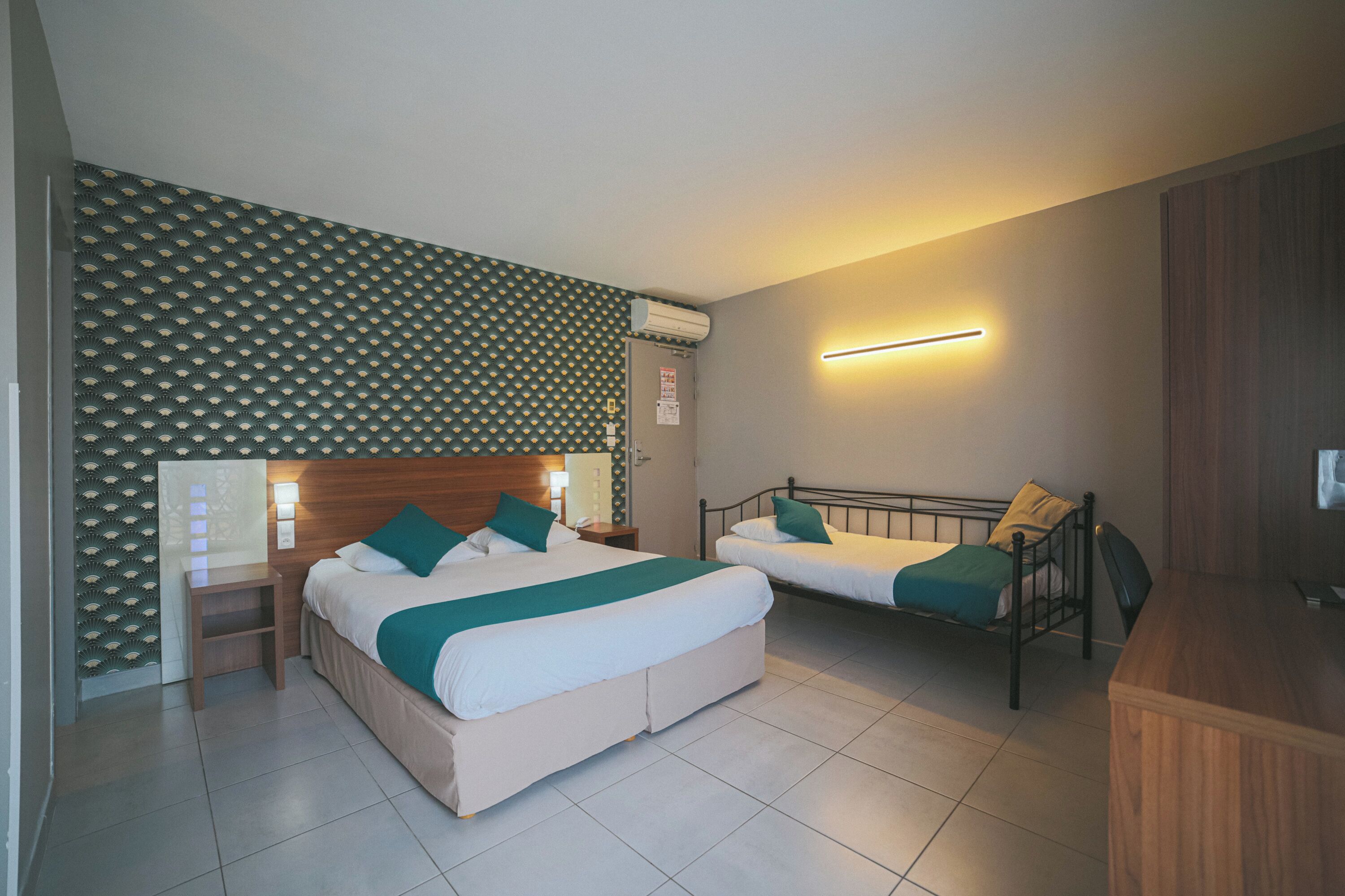 Quarto de hotel com duas camas, uma escrivaninha de madeira, ar condicionado fixado na parede e luminária.