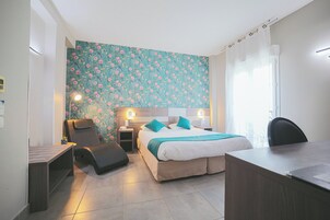 A hotel room with a bed, desk, chair, and a small seating area.