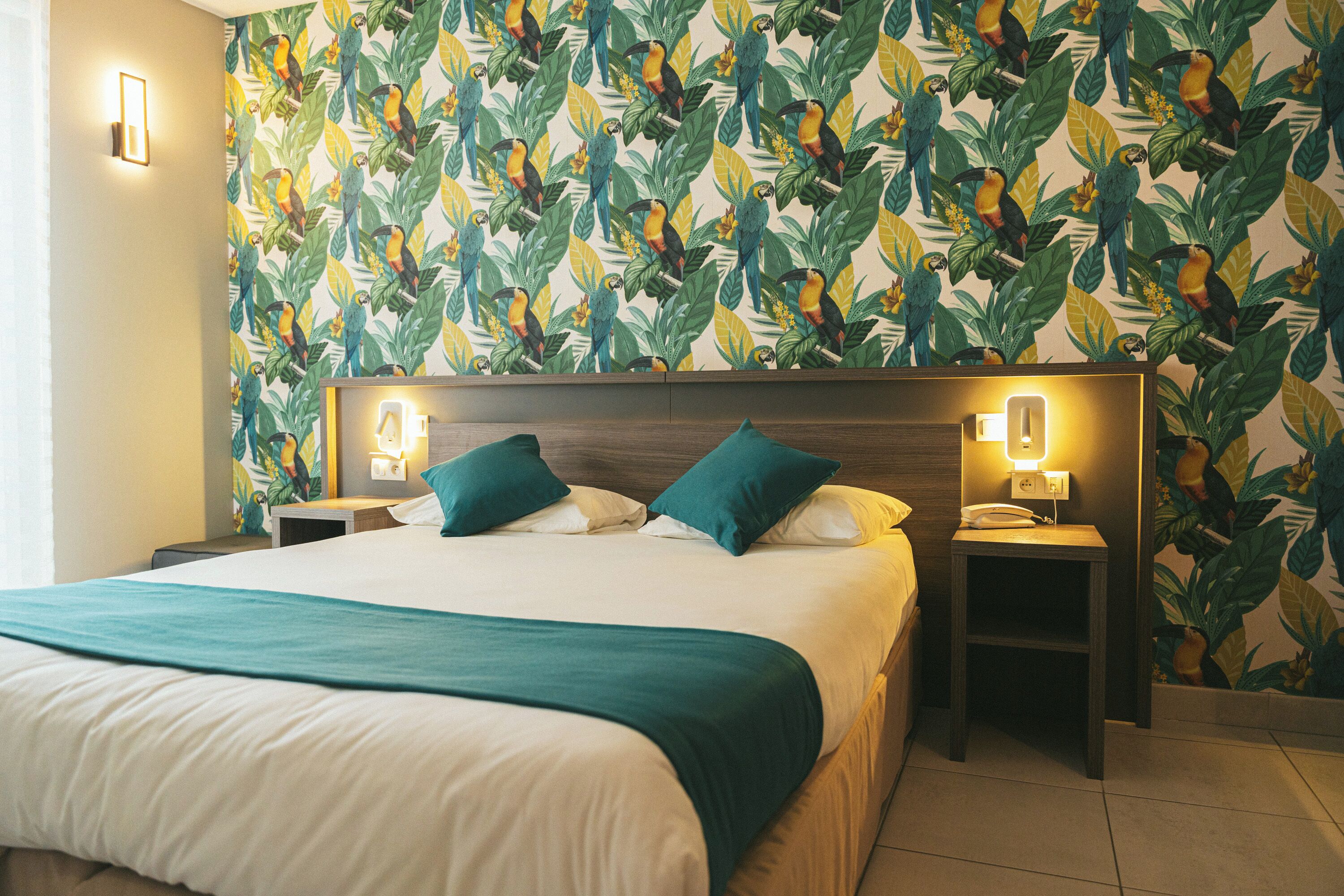 A hotel room with a large bed, two nightstands, and a wall with a tropical leaf and bird pattern.