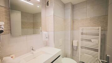 Ein modernes Badezimmer mit Waschbecken, Spiegel und Toilette. Ein Handtuchhalter und ein Fön sind vorhanden.