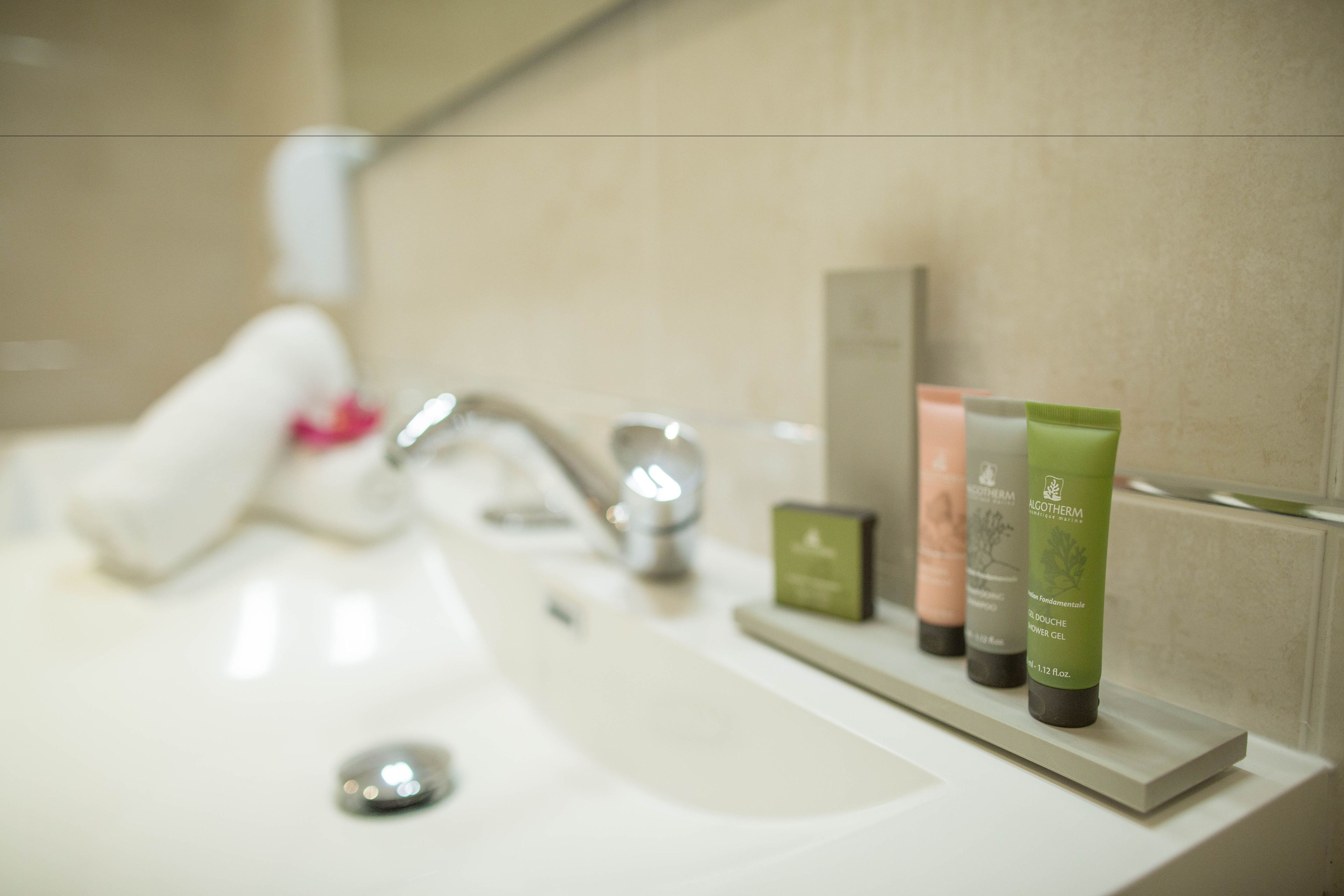 A bathroom sink with a white faucet and a mirror above it. There are three skincare products on the sink counter.