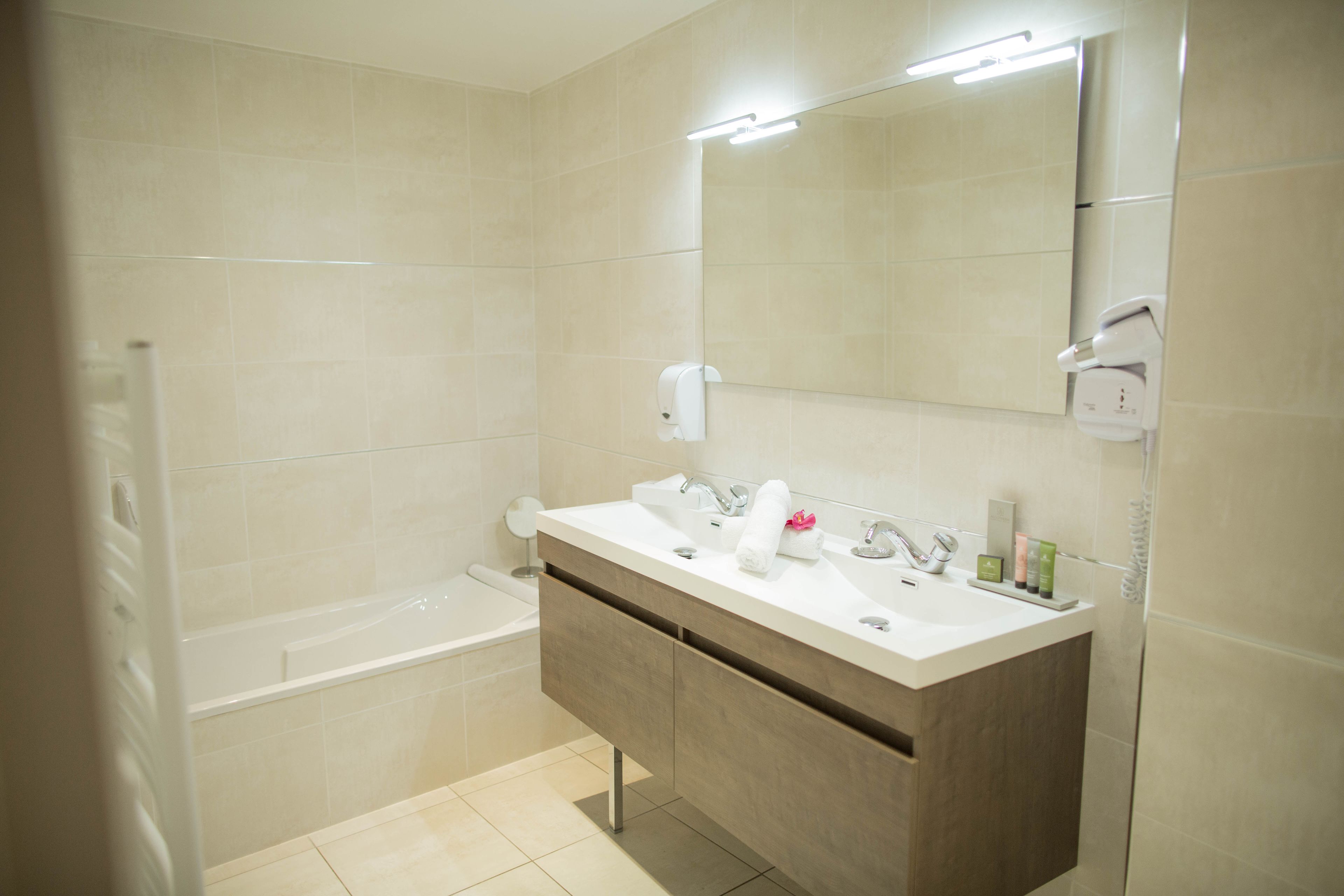 Une salle de bain moderne avec un grand miroir, deux lavabos, une baignoire et un distributeur de serviettes.