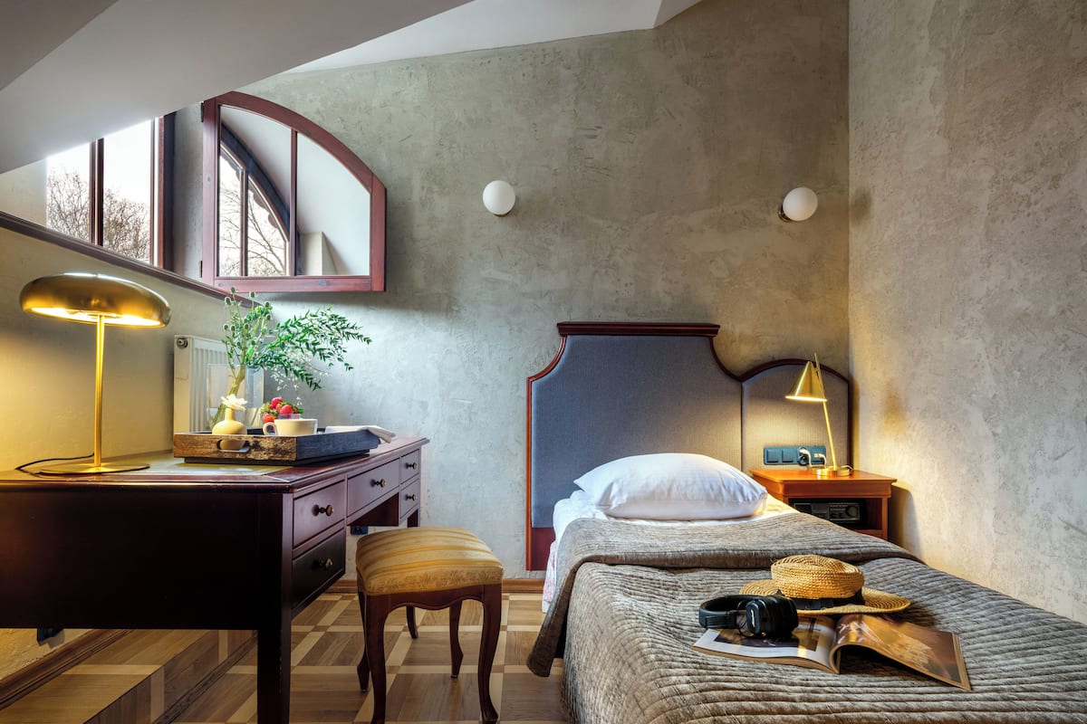 Een slaapkamer met een bed, nachtkastje, lamp, kapstok en een raam.