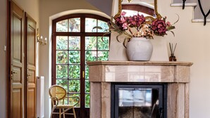 A checkered floor, a fireplace with a vase of flowers, and a chair in a hallway.