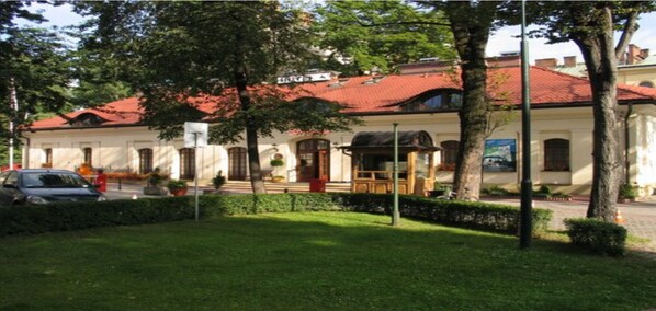 A building with a red-tiled roof, white walls, and a small garden area with trees and a bench.