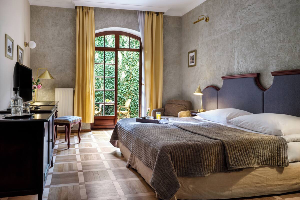 Hotelkamer met een bed, bureau, stoel, televisie en raam met gordijnen.