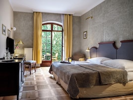 Una camera d'albergo con un letto, una scrivania, una sedia, una televisione e una finestra con tende.