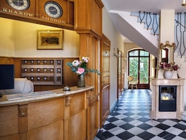 Una zona reception con una scrivania in legno, un orologio, un quadro incorniciato, un vaso con fiori e un pavimento a scacchi.