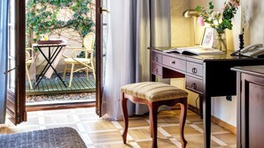 An open door leading to a balcony with a table and chairs, a desk with a lamp, a telephone, and a small stool.