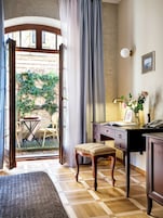 Porta aperta che dà su un balcone con tavolo e sedie, una scrivania con lampada, un telefono e un piccolo sgabello.