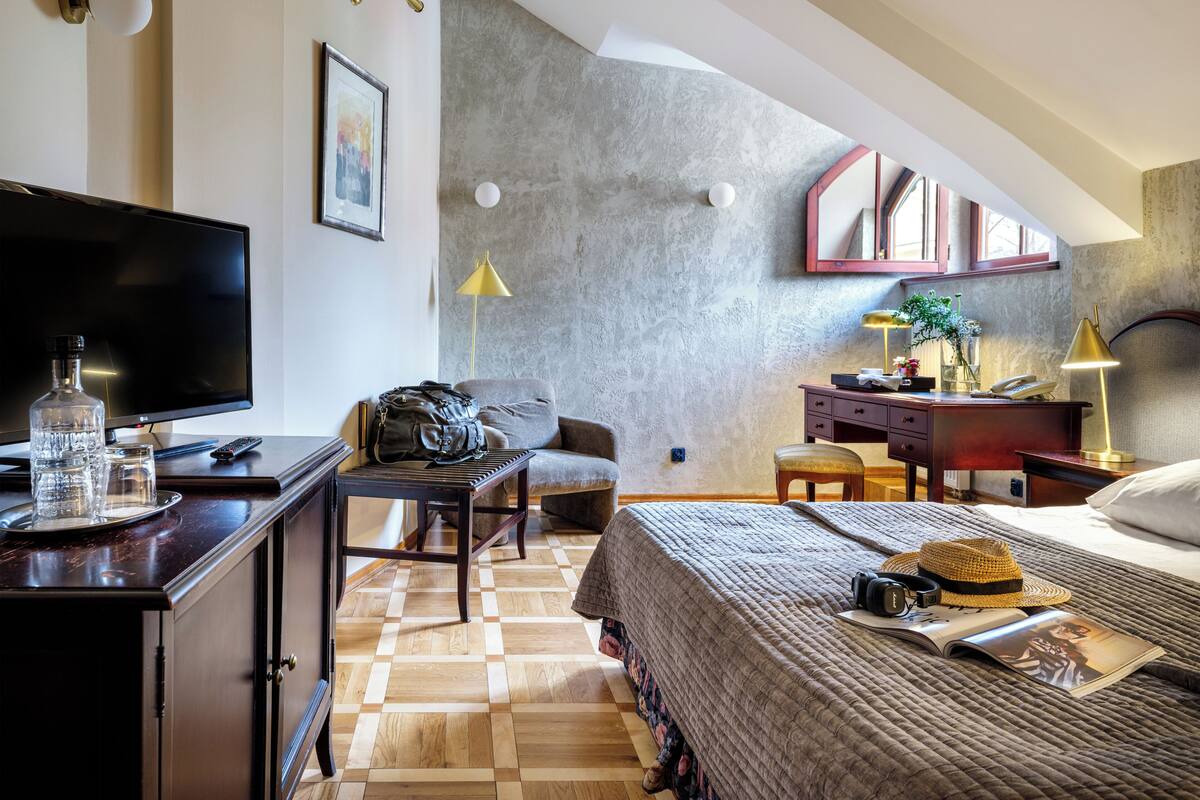 Hotelkamer met een flatscreen televisie, een bureau met lamp, een stoel, een bed met dekbed en een boekenplank.