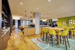 A modern kitchen with wooden cabinets, a central island, and a dining area with yellow chairs.
