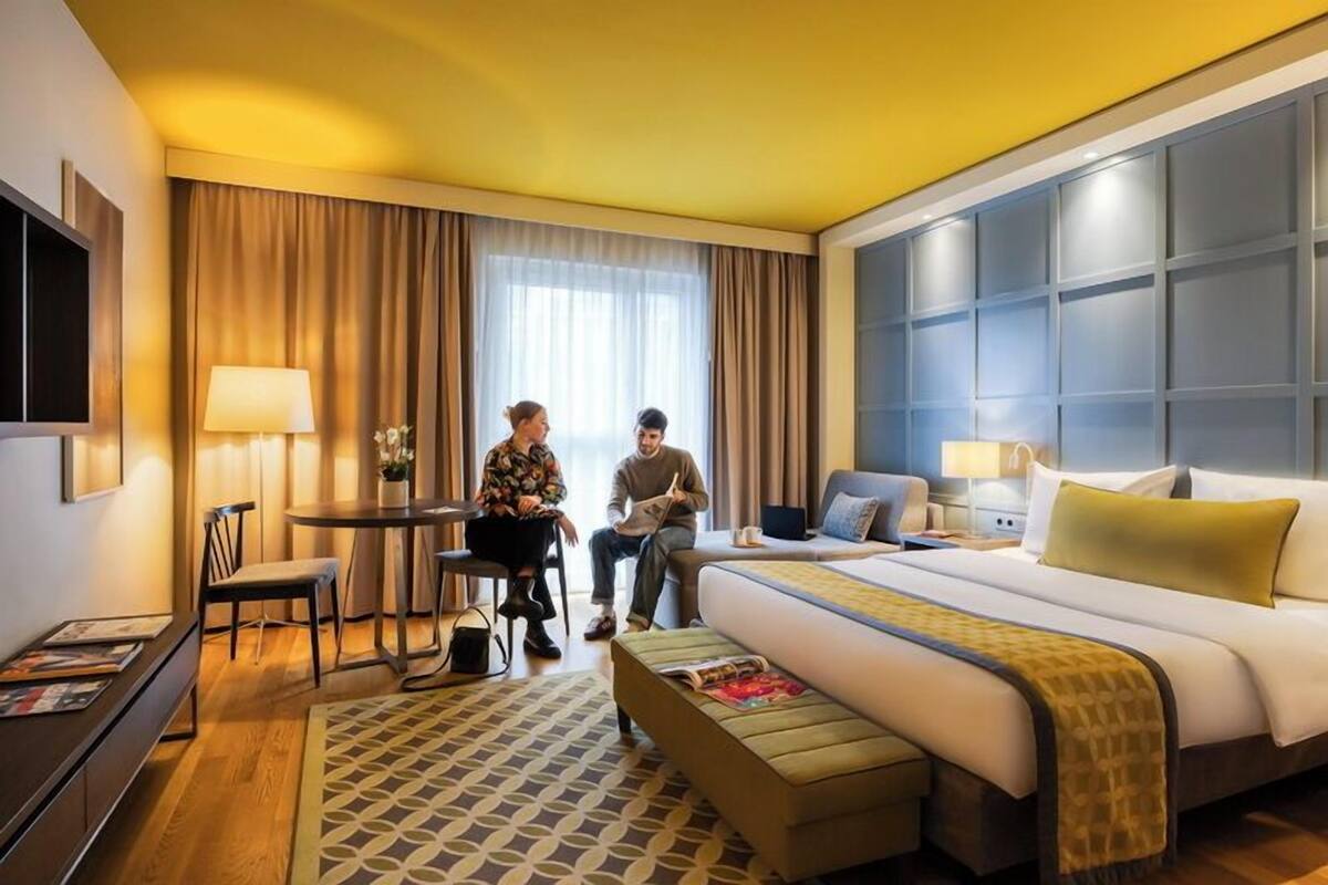 Ein Hotelzimmer mit einem großen Bett, einem Schreibtisch, einem Sessel und einem Fernseher.
