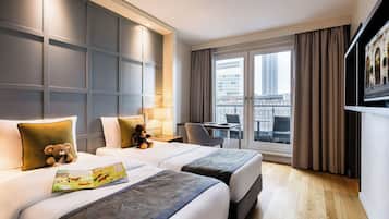 A hotel room with two beds, a desk, a chair, a window with a view of buildings, and a television on the wall.