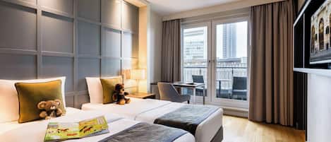 A hotel room with two beds, a desk, a chair, a window with a view of buildings, and a television on the wall.