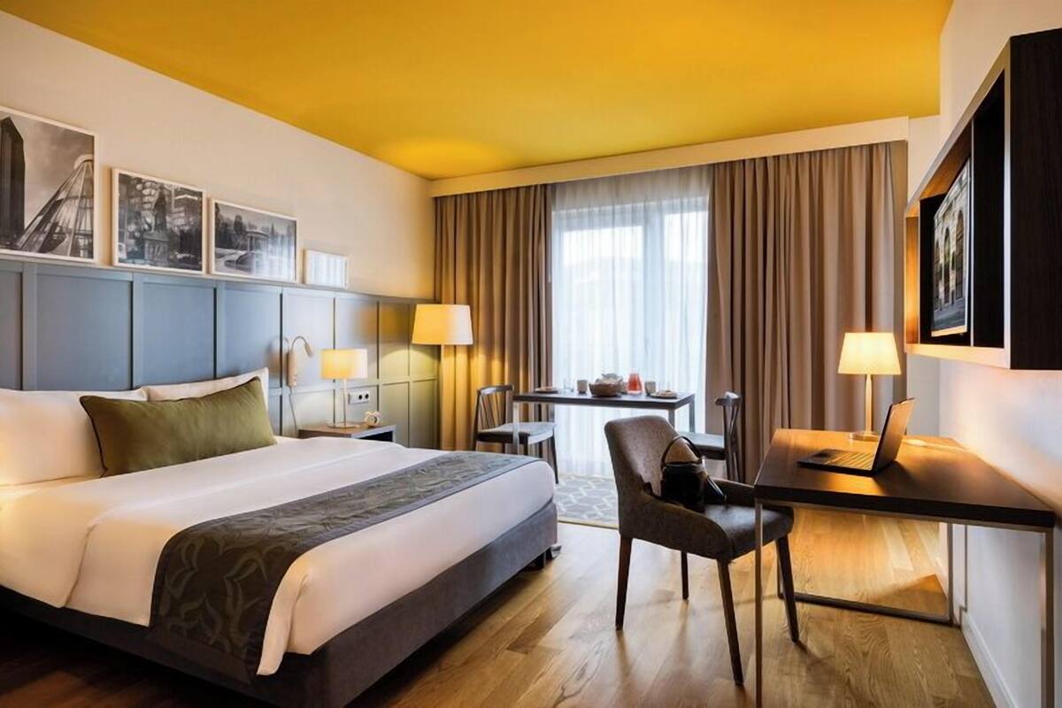Ein Hotelzimmer mit einem großen Bett, einem Schreibtisch mit einem Laptop, einem Stuhl und einem Tisch mit einer Vase.