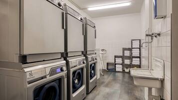 A laundry area with multiple washing machines and dryers, a sink, and a tiled wall.