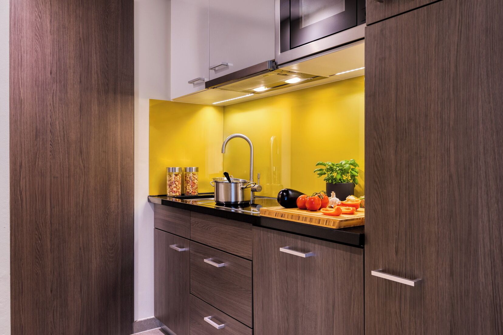 A kitchen with a yellow backsplash, stainless steel appliances, and a potted basil plant.
