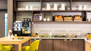 A modern kitchen with a coffee machine, breakfast buffet, and a dining area with chairs. - Citadines City Centre Frankfurt (Frankfurt)