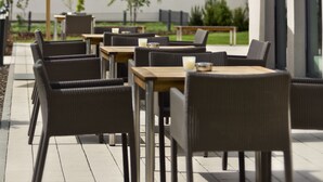 An outdoor seating area with wicker chairs and tables, a large umbrella, and a view of a building with multiple windows. - Citadines City Centre Frankfurt (Frankfurt)