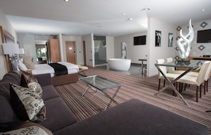 A modern hotel room with a large bed, a glass coffee table, a sofa, and a dining area with chairs. - Sketchley Grange Hotel & Spa (Hinckley)