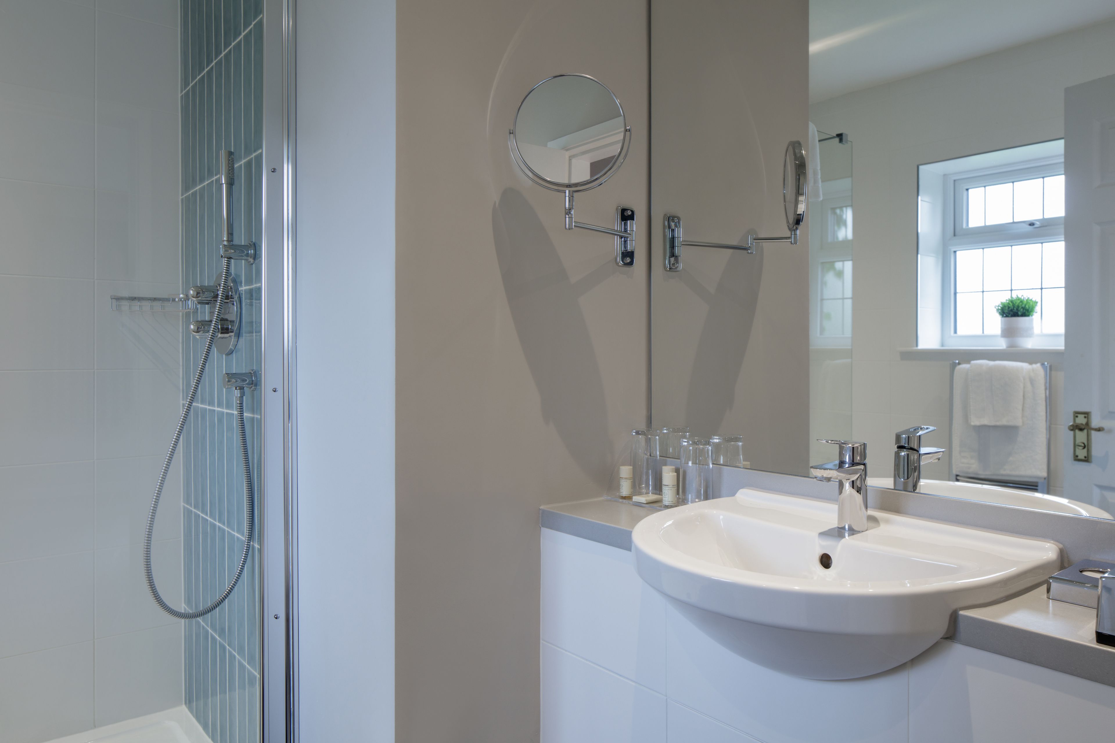 Un bagno moderno con doccia, lavandino, specchio e una finestra con una pianta.