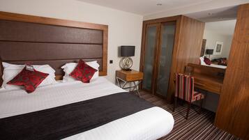 A hotel room with a large bed, a wooden headboard, a desk with a lamp, a mirror, and a striped chair.