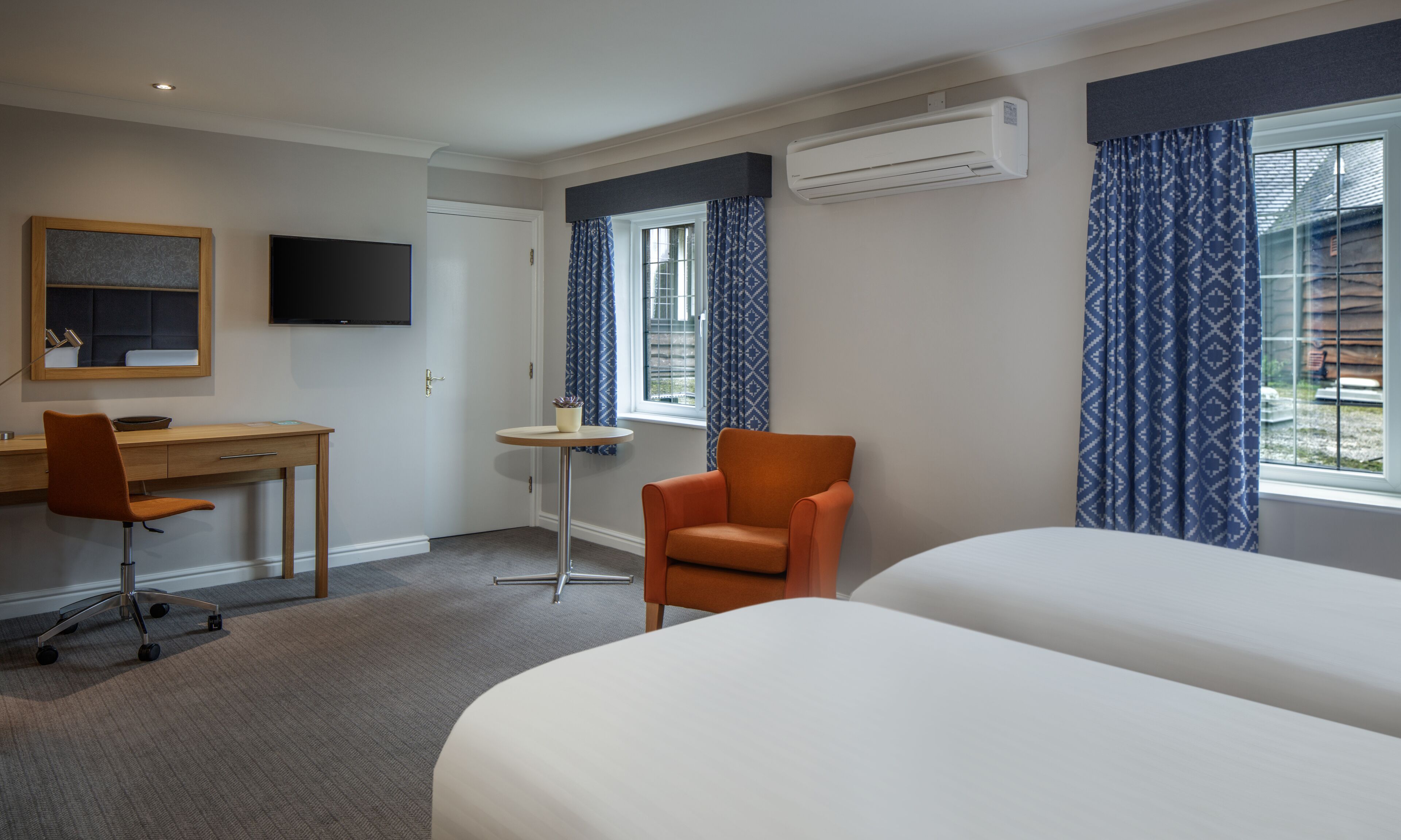 Hotellihuone, jossa on kaksi sänkyä, työpöytä, tuoli, televisio ja ilmastointilaite.