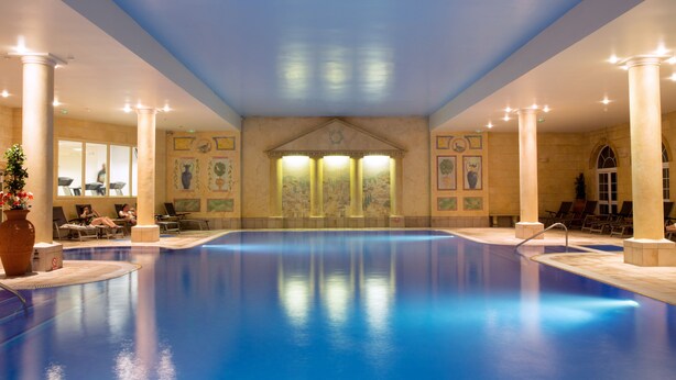 Una piscina interior con columnas, una fuente y obras de arte en las paredes.