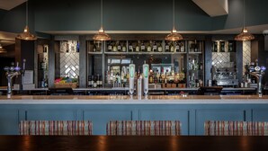 Una zona de bar con varios dispensadores de licores, estantes llenos de botellas e iluminación colgante.