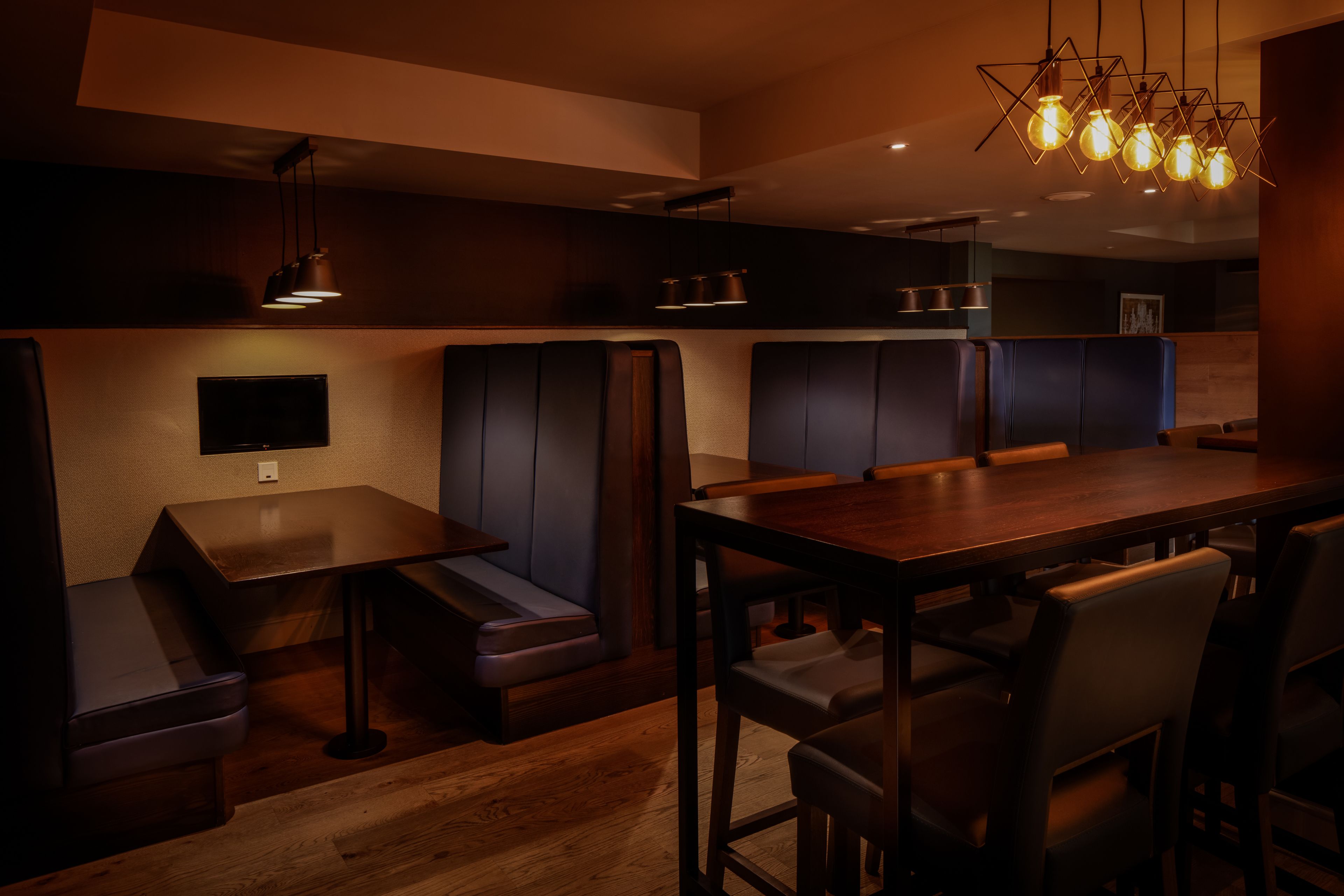 L'intérieur d'un restaurant avec des banquettes, une table en bois et des luminaires suspendus.