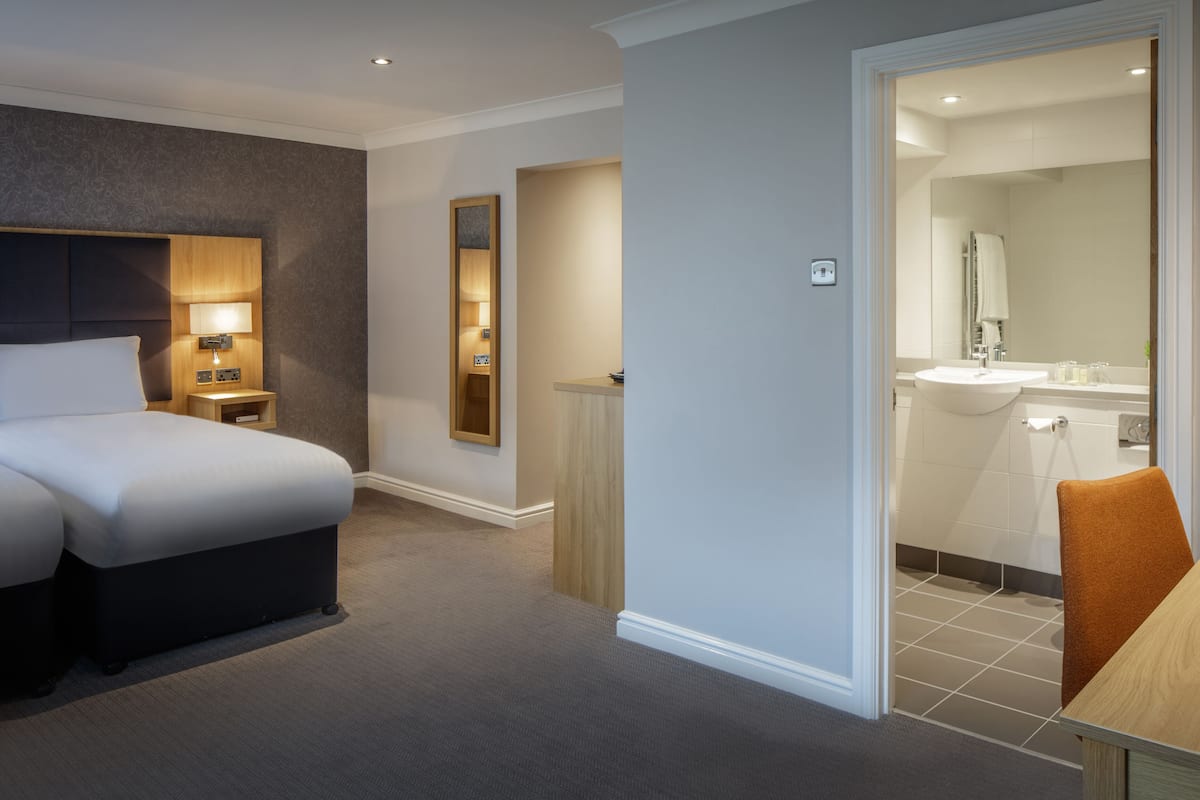 Een hotelkamer met een bed, nachtkastje, lamp en uitzicht op de badkamer.