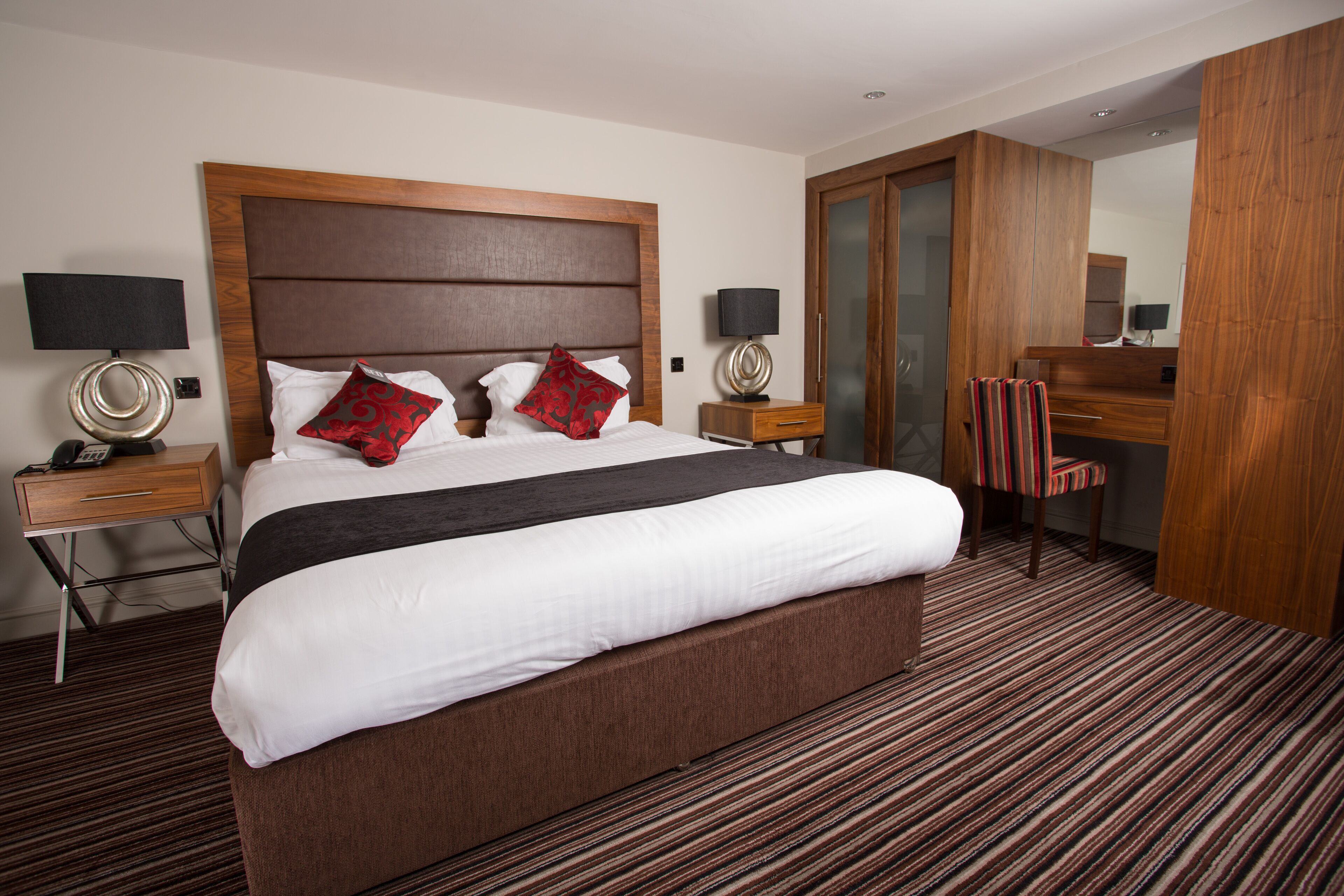 Ein Hotelzimmer mit einem großen Bett, zwei Nachttischen mit Lampen, einem Schreibtisch, einem Sessel und einem Spiegel.