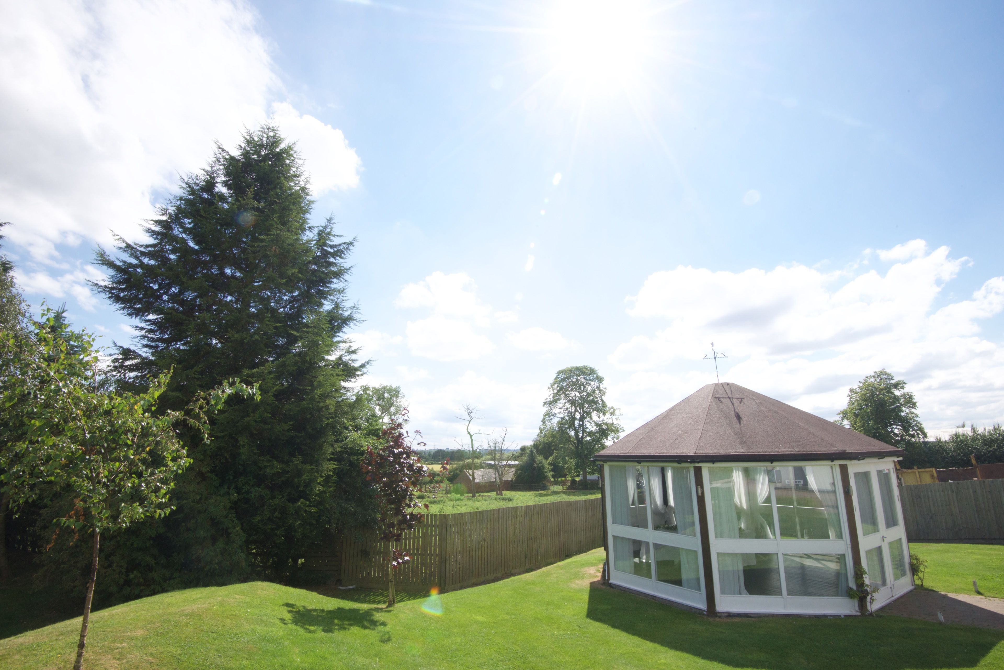 A gazebo with a peaked roof and large windows, surrounded by a well-maintained lawn and trees.