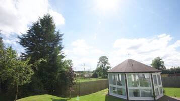 A gazebo with a peaked roof and large windows, surrounded by a well-maintained lawn and trees.