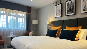 Una habitación de hotel con una cama grande, un escritorio con una silla, una lámpara y cuadros en la pared.